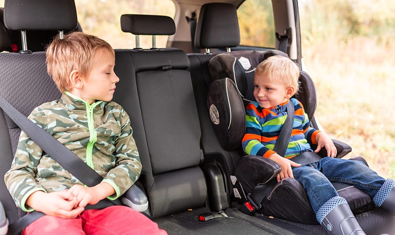 Two boys ride in booster seats in backseat of car.