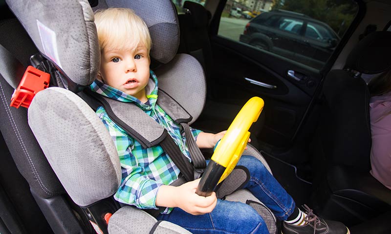Boy plays with toy in car seat.