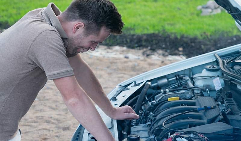 man leans over engine compartment of his car