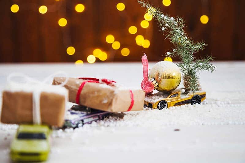 toy cars laden with Christmas balls and gifts in front of lights