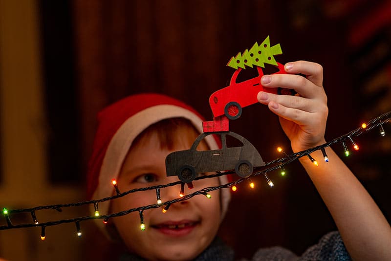young boy moves cars along strand of Christmas lights